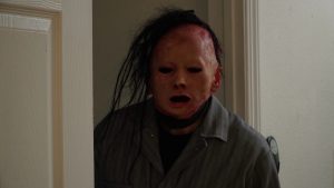 The masked killer stands by a door.