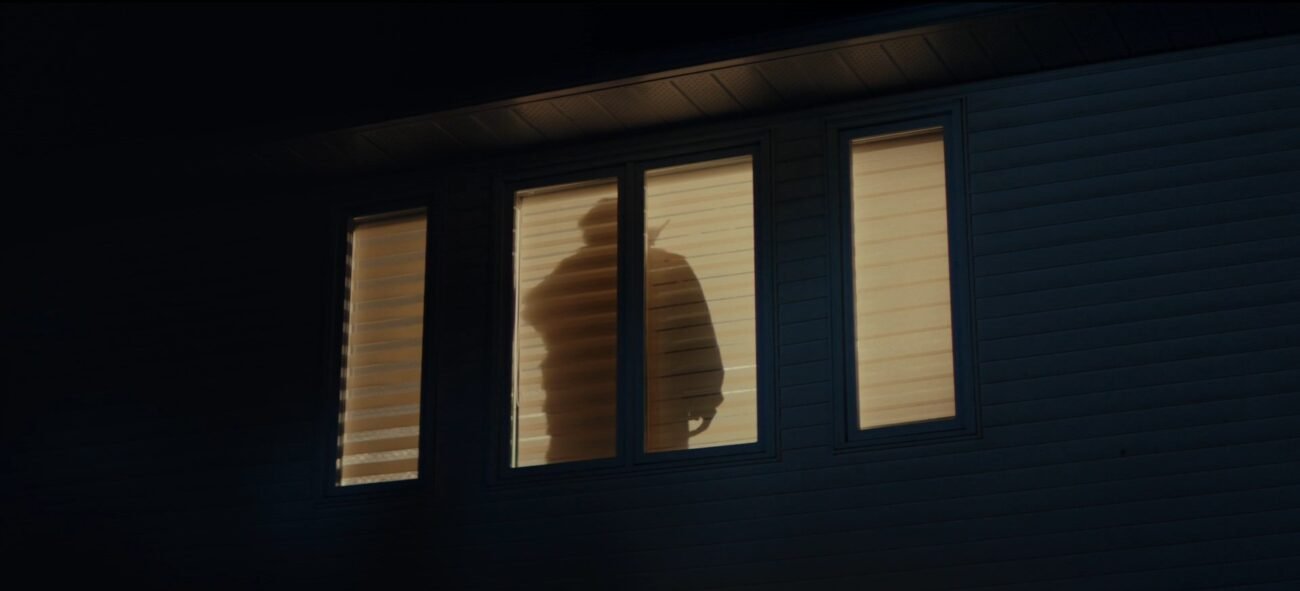 The silouette of a man holding a walkie talkie behind window blinds.